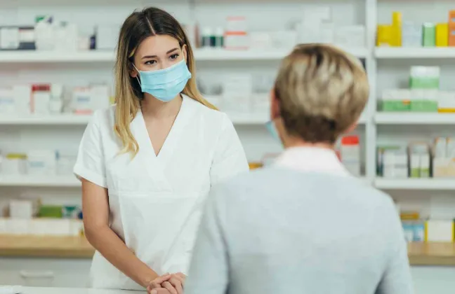 Farmacéutica con mascarilla atiende a una paciente en el mostrador farmaceutica-atiende-a-paciente