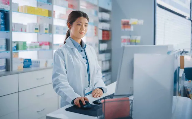 Farmacéutica utiliza el ordenador en el mostrador farmaceutica-mirando-ordenador