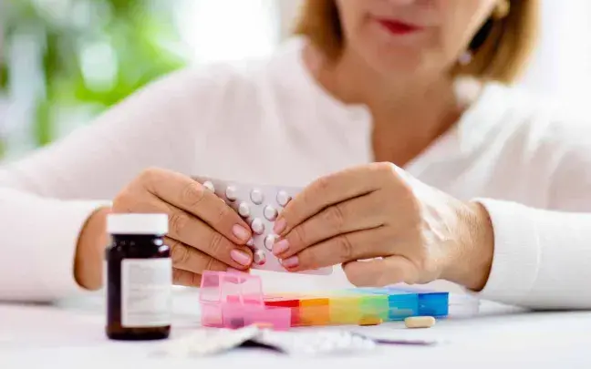 Mujer pone pastillas en el pastillero mujer-pastillero
