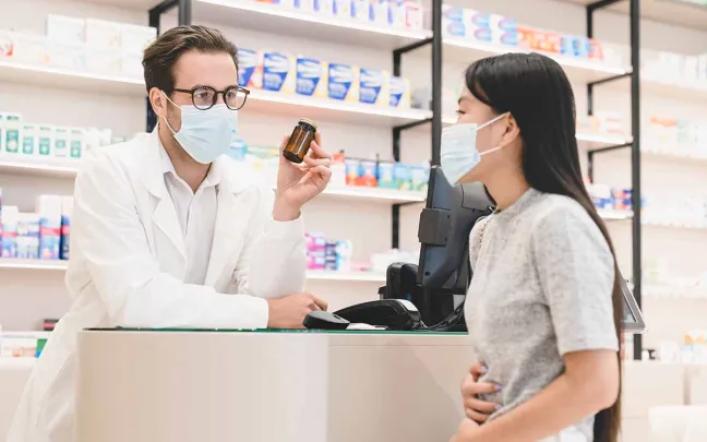 Farmacéutico en el mostrador enseña un medicamento a una paciente farmaceutico-mostrador-con-paciente