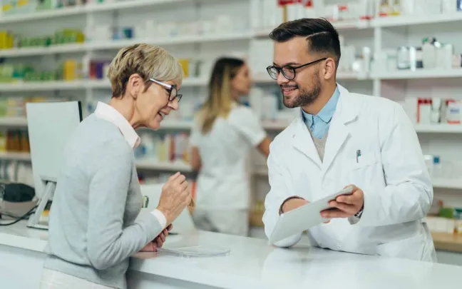Farmacéutico muestra pantalla a una paciente en el mostrador farmaceutico-y-paciente